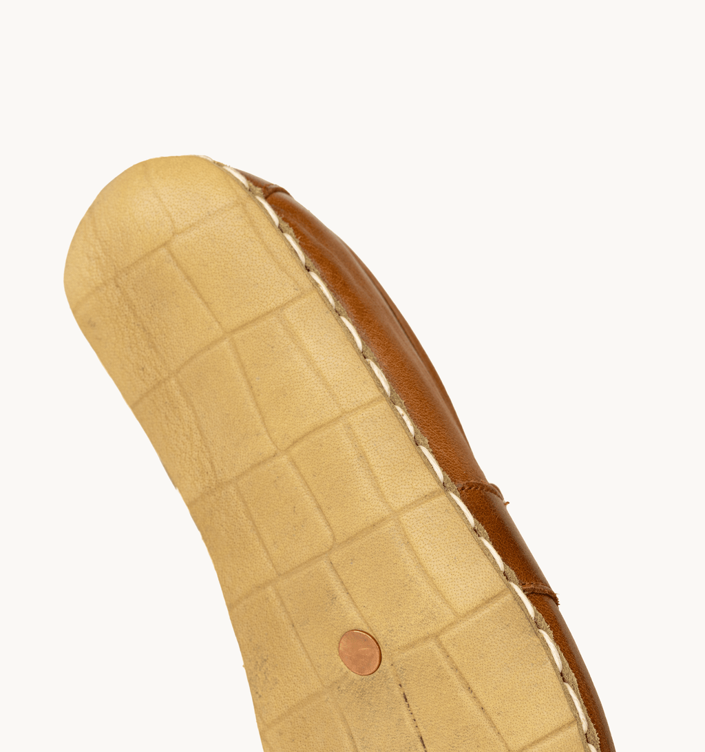 Russet men's barefoot leather penny loafer held in hand, sole and stitch detail