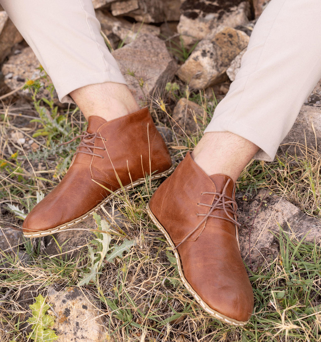 Russet men's barefoot leather chukka boot held in hand, sole and stitch detail