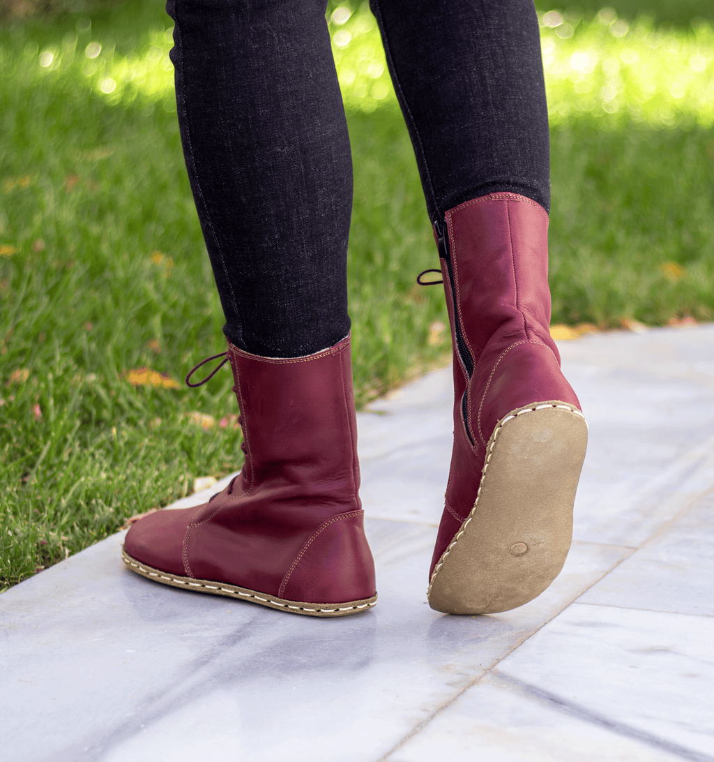 Burgundy women's barefoot leather ankle boot held in hand, sole and stitch detail