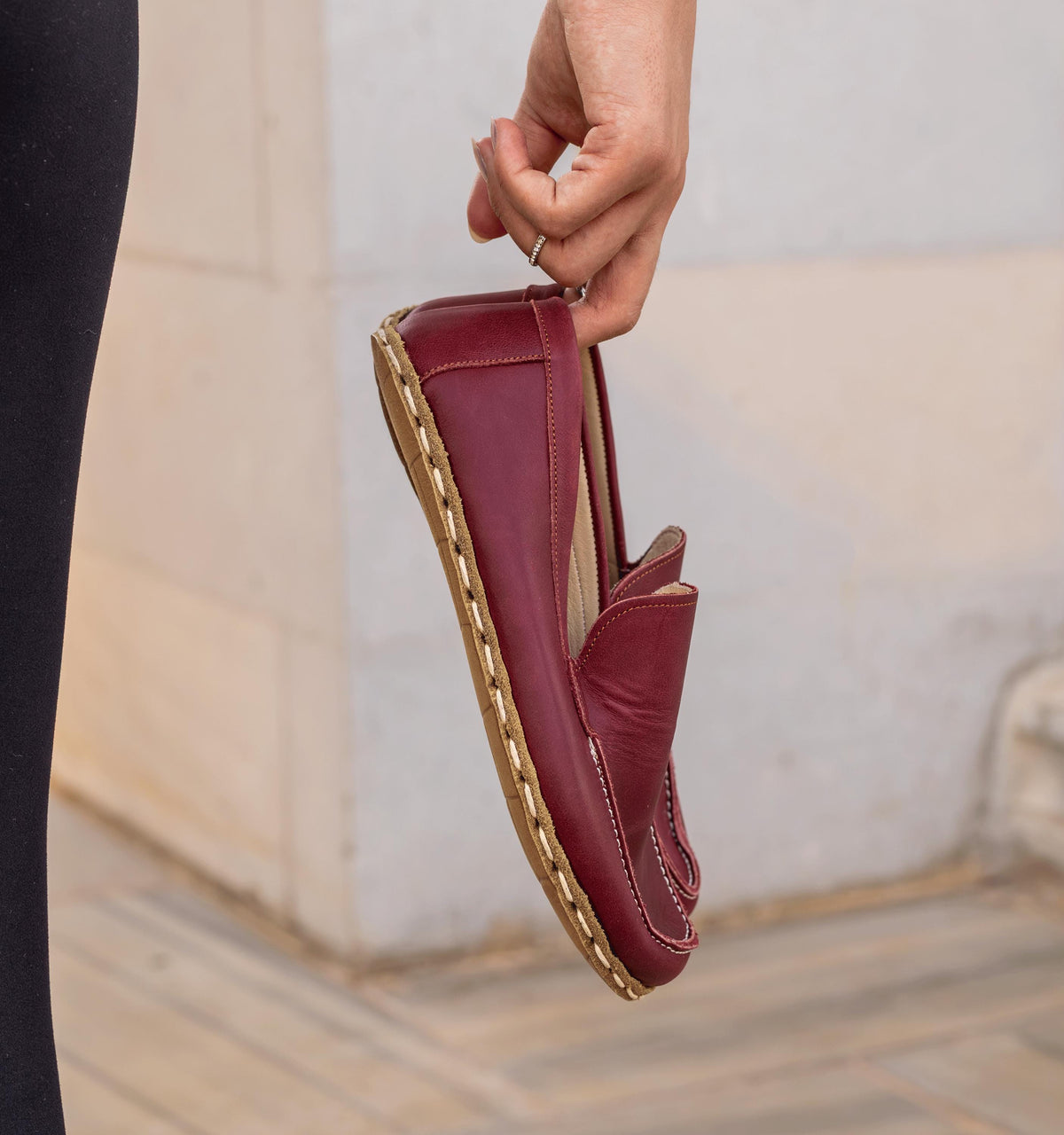 Burgundy women's barefoot leather moccasin held in hand, sole and stitch detail