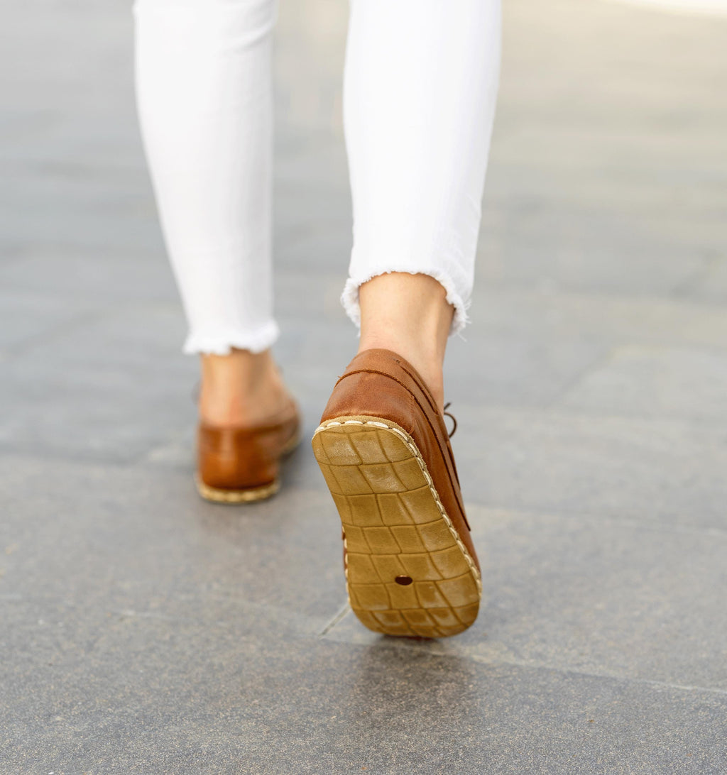 Russet women's barefoot leather boat shoe held in hand, sole and stitch detail